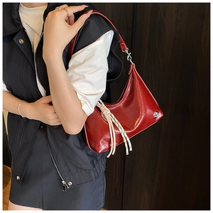Detail of red glossy leather hobo bag with pink tassel and woven rope accents