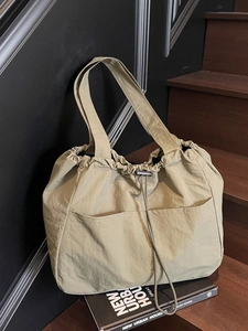 Large olive green nylon tote bag with drawstring closure and front pockets on wooden stairs