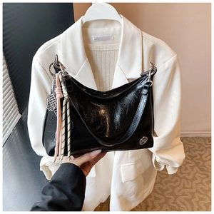 Detail of black faux leather shoulder bag with woven rope charms and tennis racket pendant