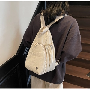Street style shot of a beige nylon backpack with drawstring pockets and sleek zippers