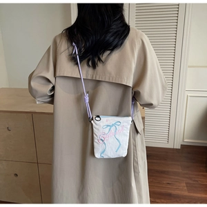 Detail of white canvas crossbody bag with blue bow embroidery and purple rope strap