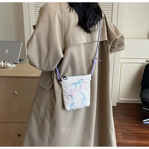 Close-up of white canvas crossbody bucket bag with ribbon embroidery and rope strap
