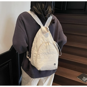 Detailed back view of a beige nylon backpack with side drawstring pockets on stairs