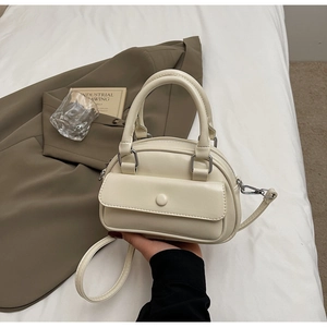 Close-up of cream-colored PU leather pillow bag featuring a curved design and front pocket