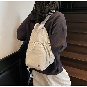 Detail of off-white nylon sling bag with front zippers and side drawstring pockets