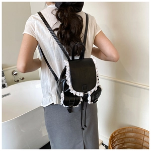 Detail view of black PU leather backpack with white lace trim worn by a model