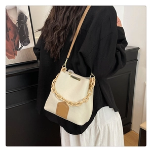 Détail du sac seau blanc cassé avec texture grainée et base en cuir marron contrastée