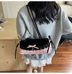 Détail du sac à bandoulière rose et noir avec nœuds et texture plissée porté par un modèle