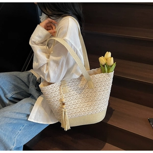 Detail of a beige woven lace tote bag with fringe charm on wooden stairs backdrop