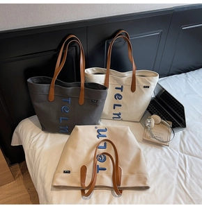Détail de sacs cabas en toile empilés en gris, beige et kaki avec anses en cuir