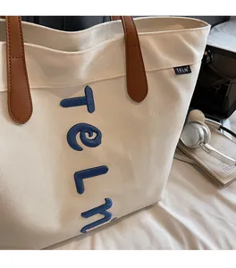 Gros plan du sac fourre-tout en toile blanche avec broderie bleue TELN et lanières en cuir