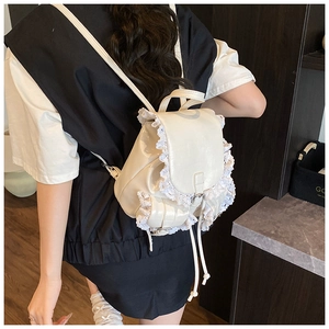 Close-up of a white patent leather mini backpack with delicate lace trim and metal buckle