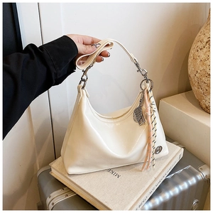 Detail of a creamy white hobo bag with shiny finish, tennis racket charm and woven tassel