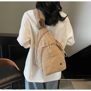 Rear view of khaki nylon backpack with dual zippers on a model in a lounge setting