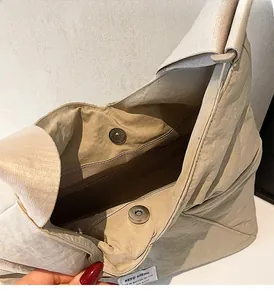 Close-up of beige nylon bag showing glossy silver magnetic clasps and smooth brown lining
