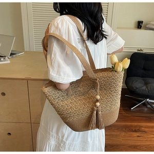 Detail of hand-woven straw tote bag featuring decorative tassels and hollow-out patterns