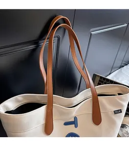 Détail du sac fourre-tout en toile blanche avec bandoulières en cuir et étiquette TELN