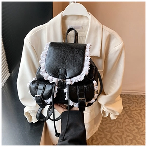 Detail of black faux leather backpack featuring white lace trim and silver buckle pockets