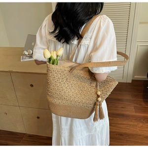 Model wearing a beige straw tote bag with lace crochet details and a wooden bead tassel