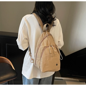 Rear view of khaki nylon backpack on model showing adjustable straps and multi-pocket layout
