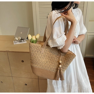 Detail of woven straw tote bag featuring hollow floral pattern and beaded tassel accent