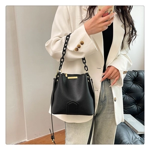 Détail du sac seau noir en cuir grainé avec finitions dorées porté sur une veste beige