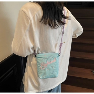 Detail view of a light blue canvas crossbody bag with purple rope strap and bow embroidery