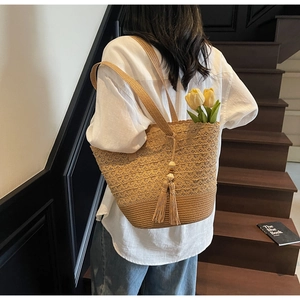 Detail of woven straw tote bag featuring decorative wood beads and boho tassels