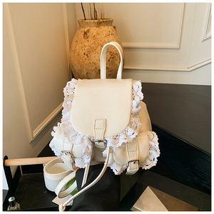 Detailed view of white faux leather backpack featuring elegant lace trim and silver buckles