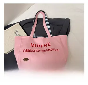 Close-up of pink canvas tote bag with red typography and striped handle details