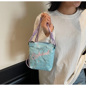 Detail of light blue canvas crossbody bag featuring pink bow embroidery and rope strap