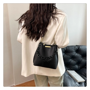 Détail du sac seau noir texturé avec accents dorés et chaîne en résine porté par le mannequin