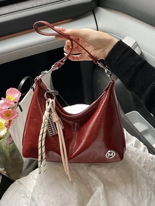 Glossy burgundy shoulder bag with M logo and decorative charms in a car interior