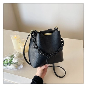 Gros plan d'un sac seau noir en cuir grainé avec chaîne décorative et garnitures dorées