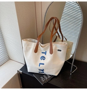 Détail de la broderie et des poignées en cuir marron sur le sac cabas en toile crème