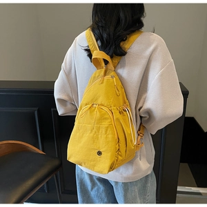 Detail view of mustard yellow teardrop backpack featuring multi-pocket design on model