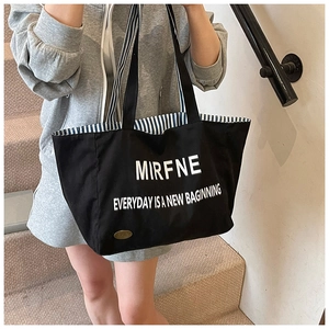 Detail of black canvas tote bag with white lettering and gold metal logo charm
