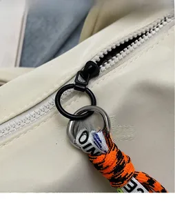 Close-up of smooth metal zipper with orange braided strap on beige nylon bag