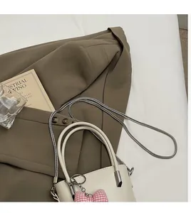 Detail der cremeweißen Beuteltasche mit silberner Kette und rosa Schleifenanhänger