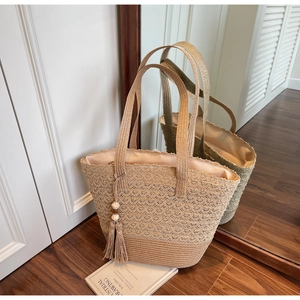 Close-up of beige woven straw tote bag featuring detailed hollow-out texture and tassels