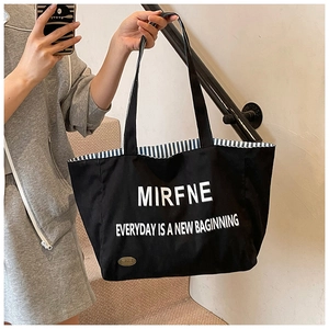 Detail of black canvas tote showing letter print and blue striped interior lining