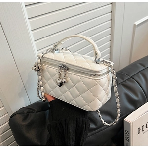 Detail of white quilted crossbody bag with silver chain and heart charm accessory