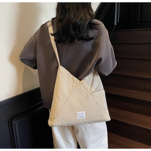 Detailed view of beige nylon crossbody bag with branding label worn on staircase