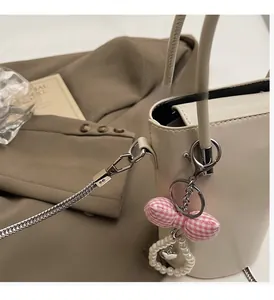 Detailansicht der cremefarbenen Ledertasche mit Silberkette, Karoschleife und Herzanhänger