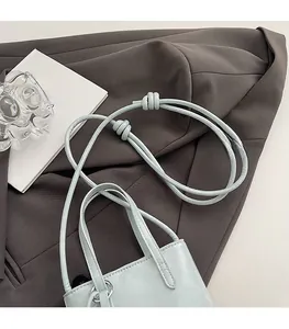 Detail of light blue leather bucket bag with knot shoulder strap on gray suit fabric