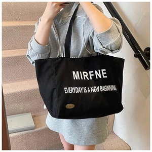 Detailed shot of large black canvas tote bag featuring white letters and golden metal logo