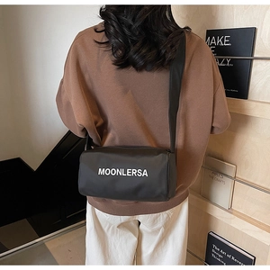 Rear view of a black canvas cylinder bag with Moonlersa print and wide strap on model
