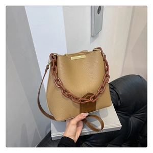 Détail du sac seau en cuir à motif litchi avec chaîne acrylique et garniture dorée