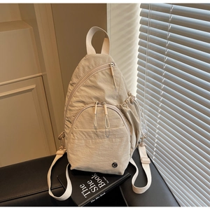 Detail view of beige nylon backpack featuring multiple zip pockets and adjustable strap