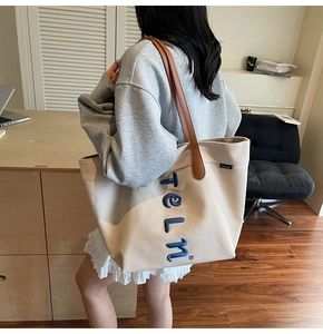 Détail du sac cabas en toile beige avec broderie bleue et anses en cuir marron